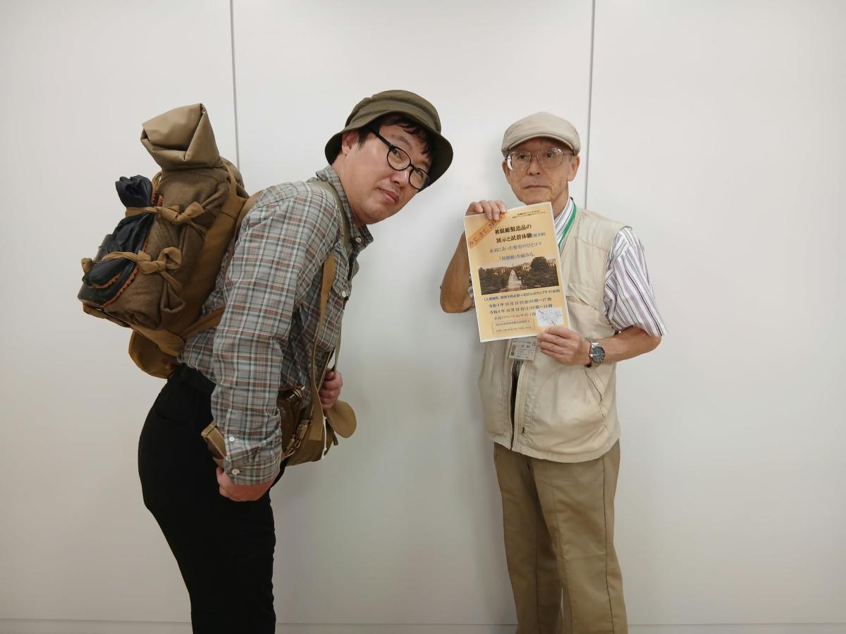 装備品を背負う杉山英一さんとチラシを手に来館を呼びかける上野基次さん