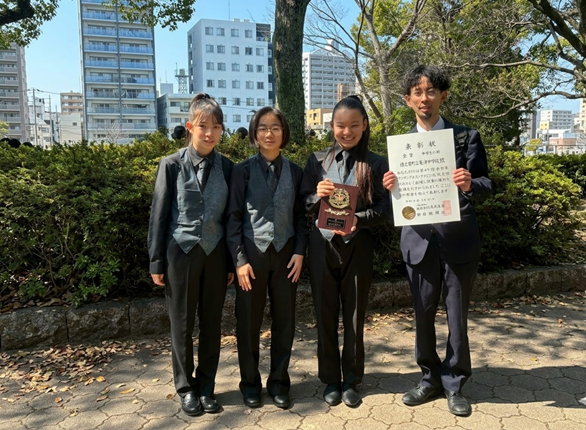 大島紬の衣装で大会に臨み、見事、金賞に輝いた亀津中学校吹奏楽部の3人と顧問の宇都教諭（写真提供＝井望美さん）