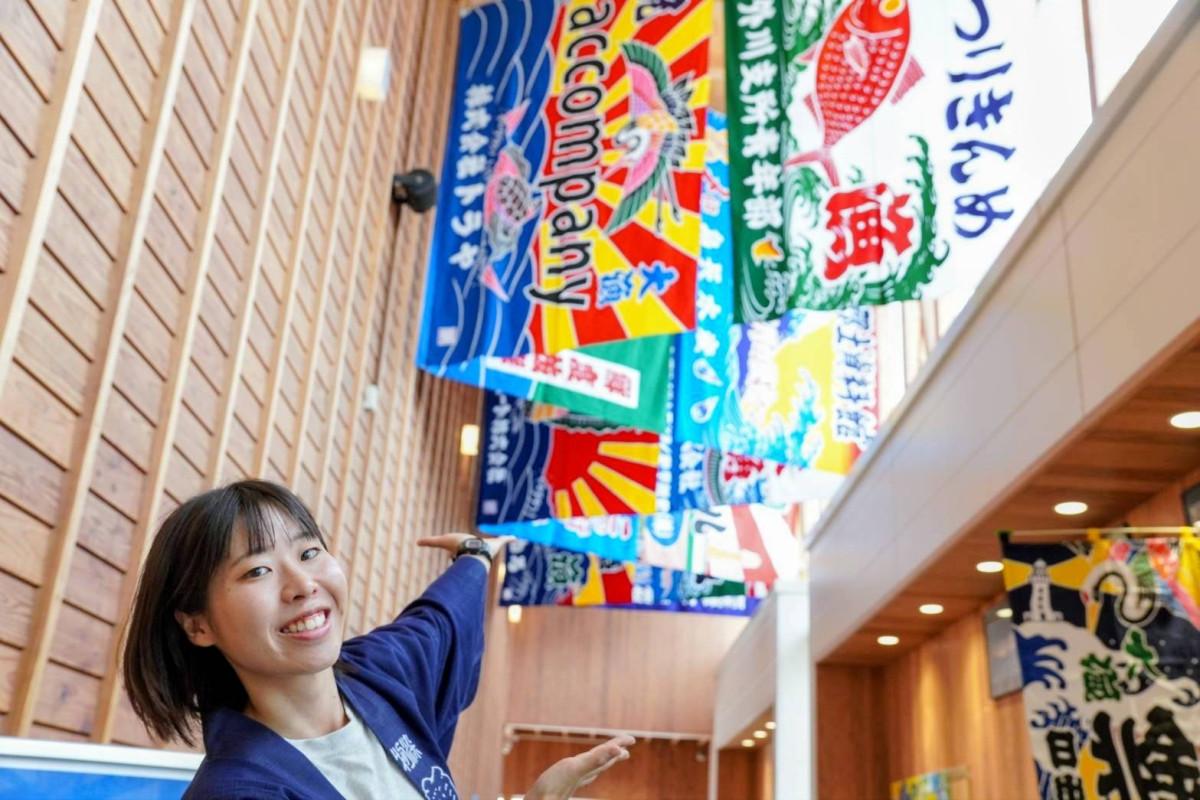 プロジェクト発起人の山嵜さんと銚子駅構内に掲げられた大漁旗