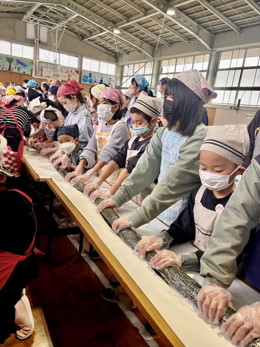 藤木小学校の全校児童61人が2列になって、長さ13メートルのジャンボのり巻きを巻いた