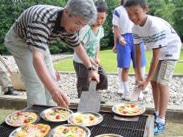 ドラム缶で作ったピザ窯でピザを焼く参加者ら