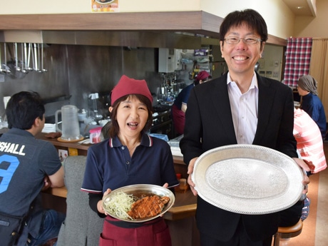 レギュラーサイズの金沢カレーを手にする｢まつや｣店長の扇田さん（左）と、ジャンボ用の皿を手に挑戦者を呼び掛ける｢ケービーエフ｣社長の東さん（右）