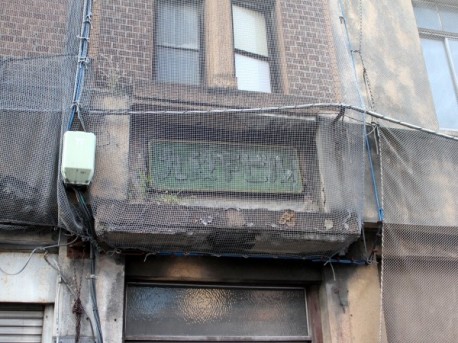 ビル名が刻まれたプレート。建物の外壁が落ちてくるのを防ぐネットがかけられていた