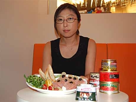 コンビーフ缶を丁寧に盛り付けた「缶詰メニュー」を手にするタカイさん。テーブルには「コレクション」の一部で2,000円以上する高級缶詰も