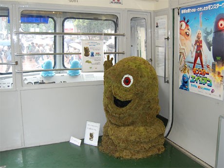 東急5000系車内に登場した「グリーン・ボブ」。車内には映画「モンスターVSエイリアン」のポスターも