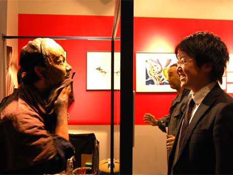 若木くるみさんの最新作「お面」のライブパフォーマンス。ハーフミラー越しに若木さん扮（ふん）する岡本太郎（左）、観客（右）が対峙（たいじ）し、刻々と顔が塗り替えられていく