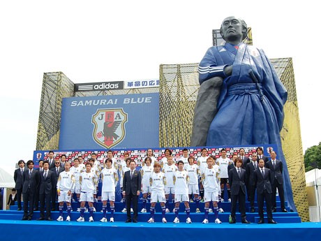 日本代表のユニホームをモチーフにした巨大龍馬像をバックにしたサッカー日本代表の23選手と岡田武史監督、エグザイルのメンバー