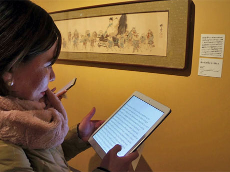 多言語ガイドタブレットを手に展覧会を回る外国人来場客