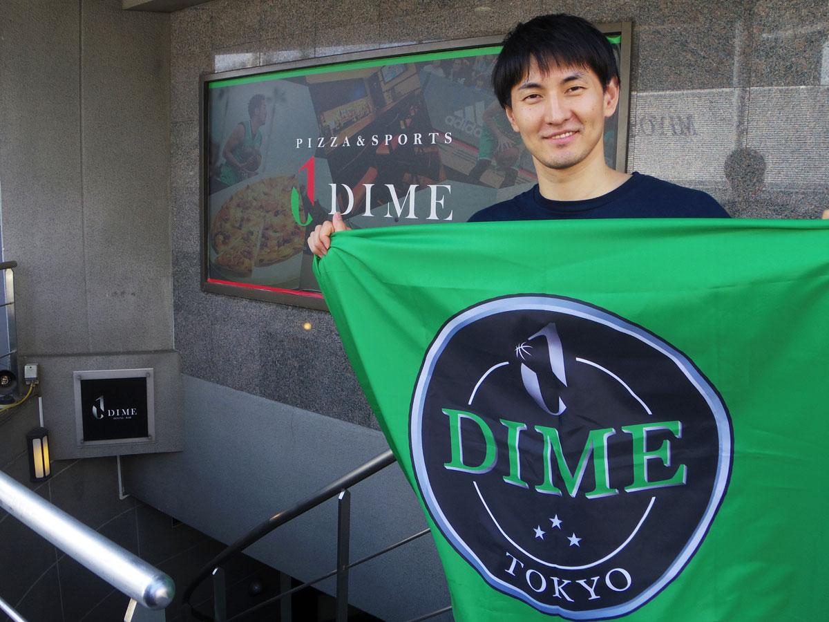 渋谷のスポーツバー「DIME」前でチームフラッグを掲げるオーナー兼選手の岡田優介さん