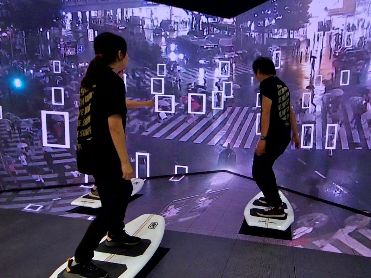 スクランブル交差点を渡る人の量などを解析し作るデジタルの波と連動してサーフボード型のデバイスが動く
