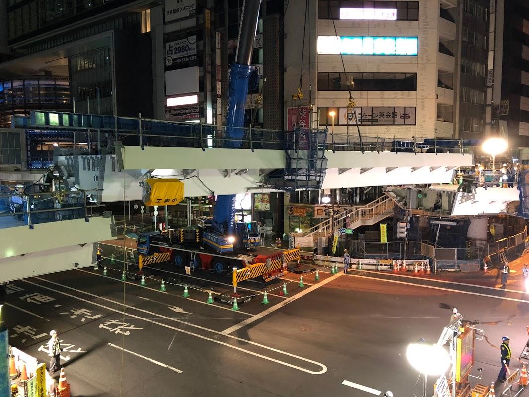 クレーンでいったん持ち上げられた巨大な橋桁が下ろされて両端の既存の橋の間にはめこまれていく
