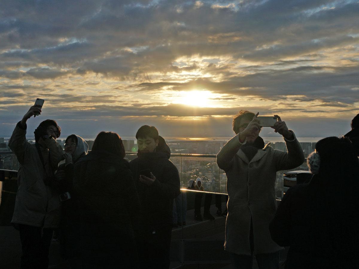 雲の切れ間からのぞく初日の出の写真を撮る来場者ら