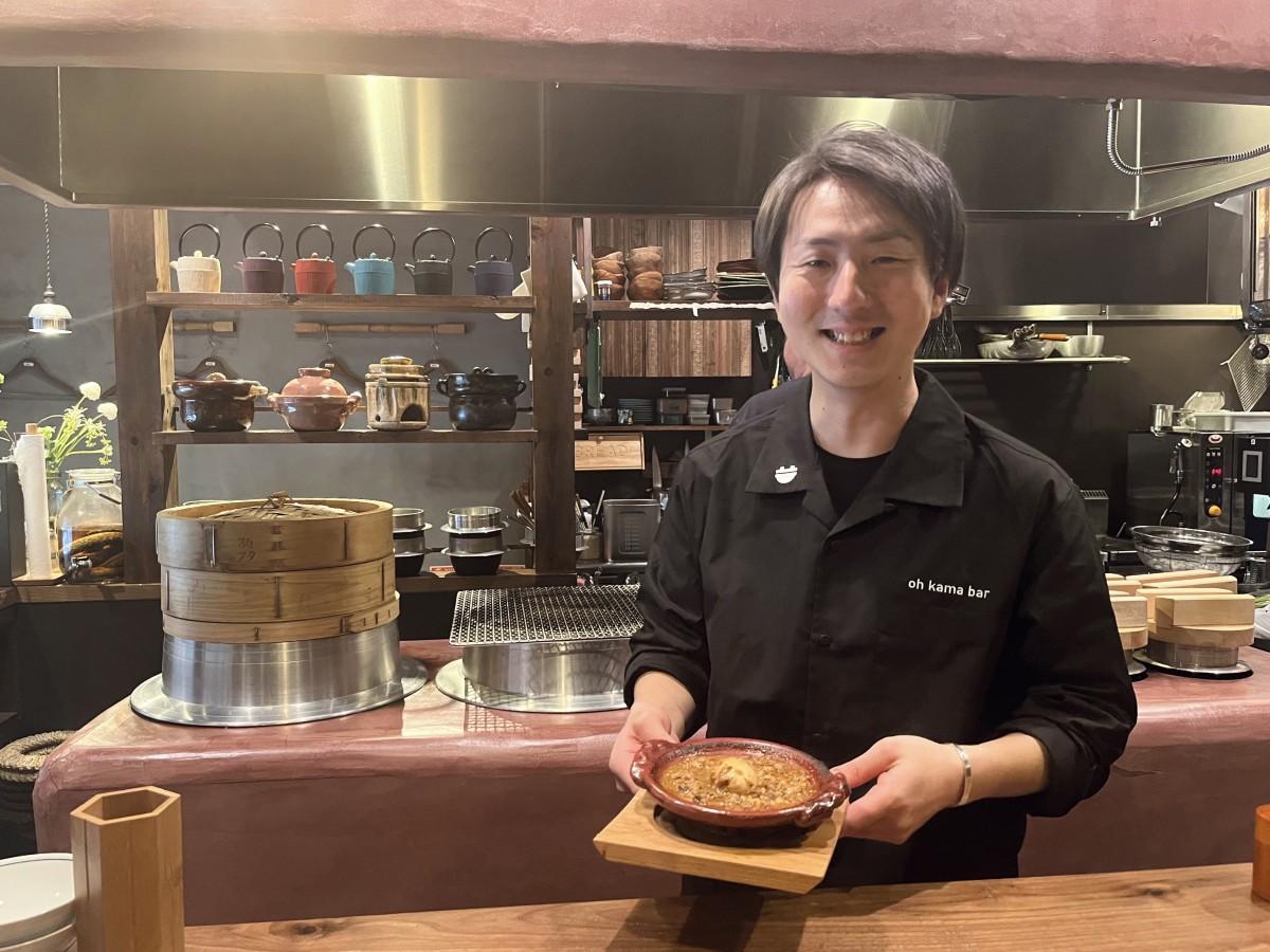 土釜の煮込みを手にした伊藤大輔店長。カウンター内には特注のかまども