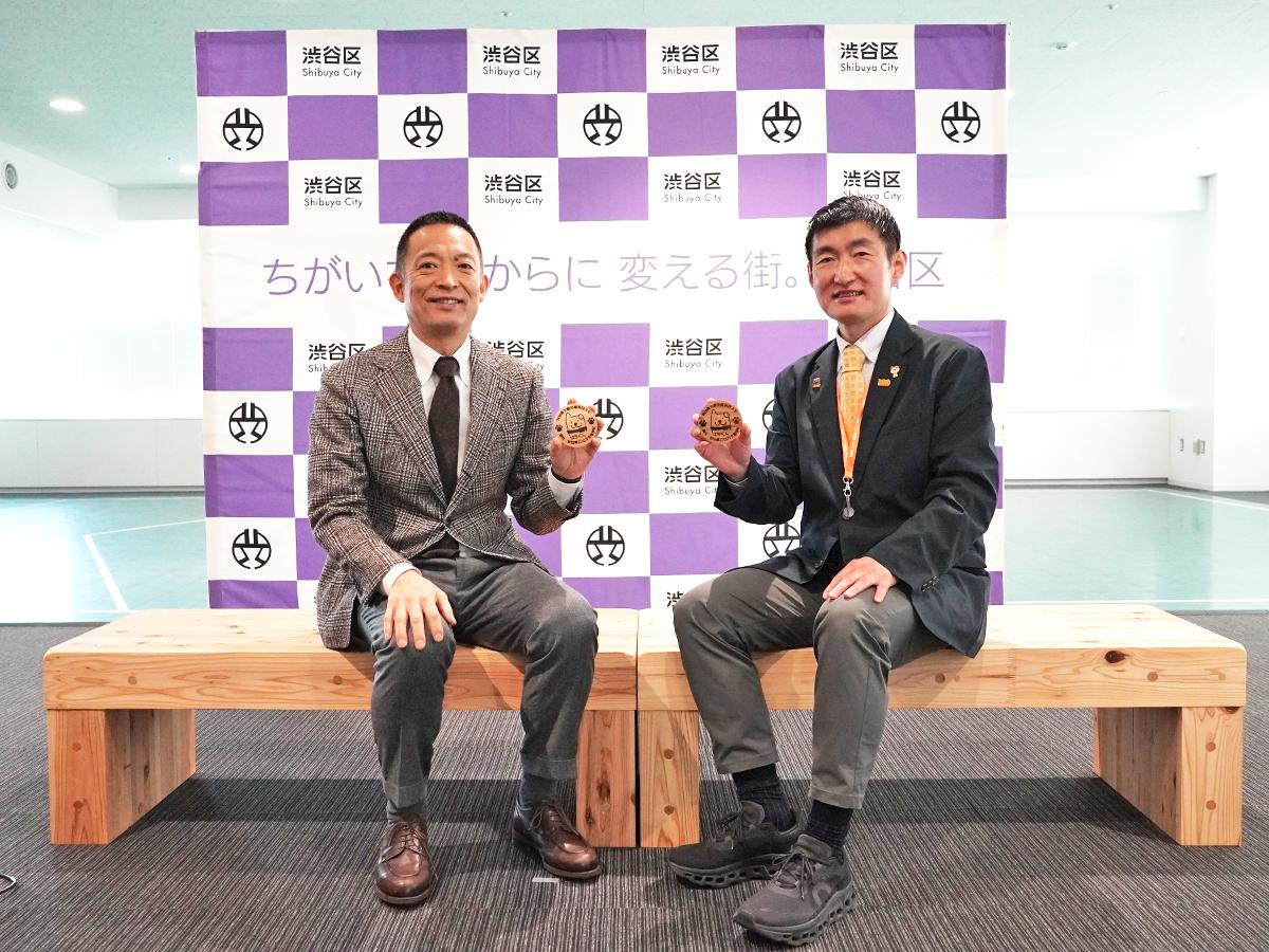寄贈されたベンチに腰をかける（左から）長谷部健渋谷区長と福原淳嗣大舘市長