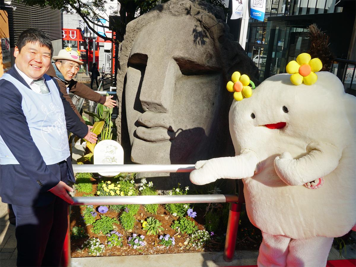 モヤイ像前でポーズを取るシブハナ代表の小島盛利さん（写真手前）、マスコットキャラクターの「くもっくる」ら