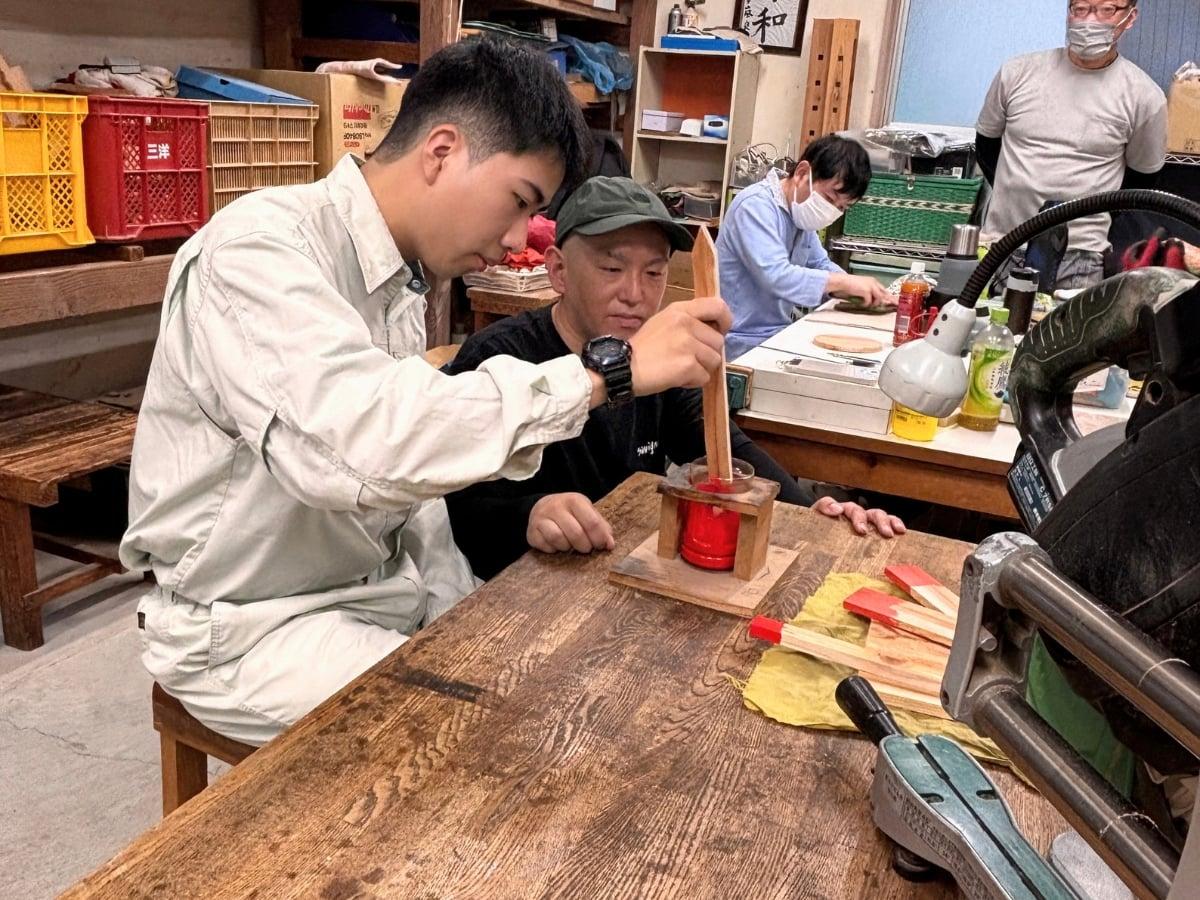 木杭の先端部を赤い塗料に浸して塗装する作業の様子