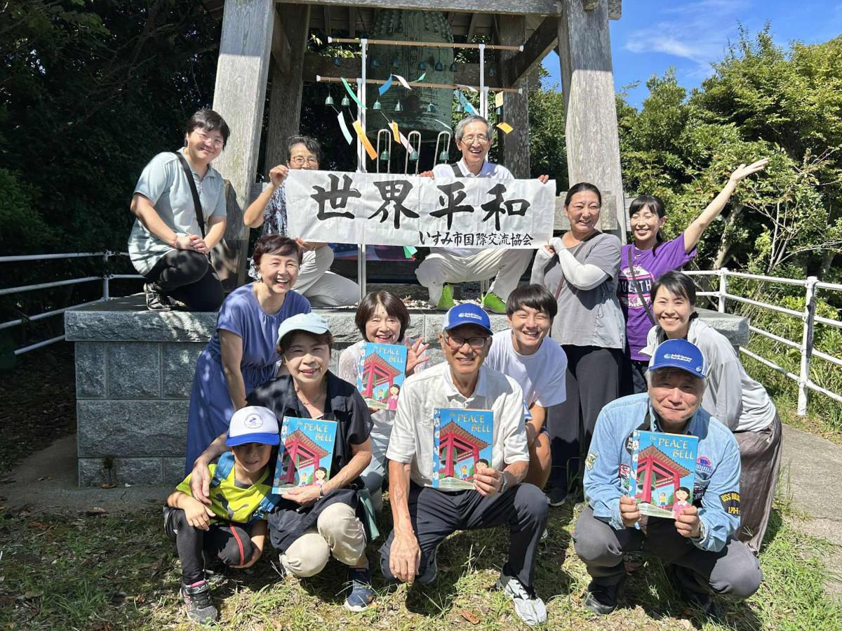 史実に基づきアメリカの児童文学者マギ・プリウスさんが出版した「The PEACE BELL」と共に記念撮影した参加者（日本語版は市内の井上書店で購入可能）