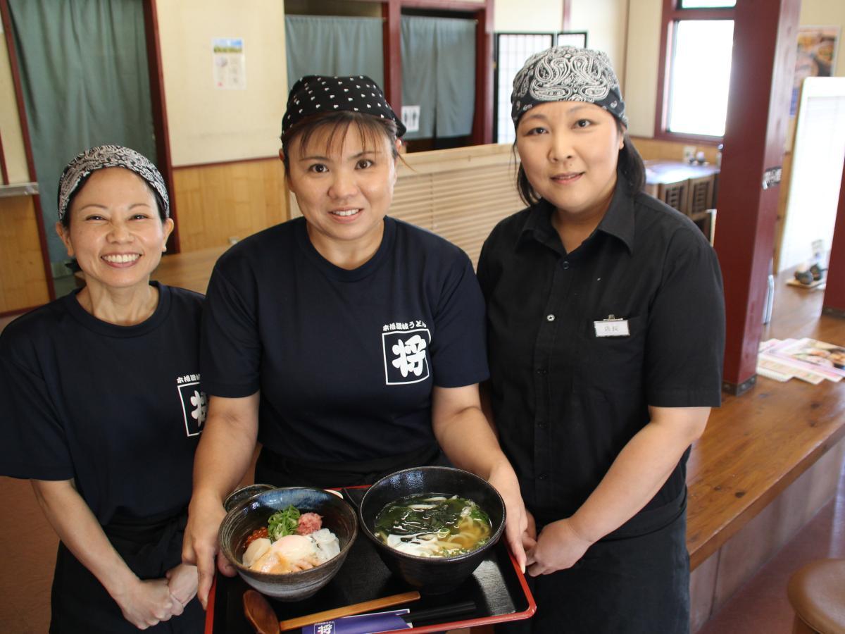 1周年記念の丼とうどんのセットを持つ店のスタッフ