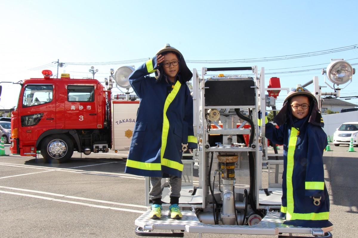 消防服を身にまとってはしご車の体験をする兄弟