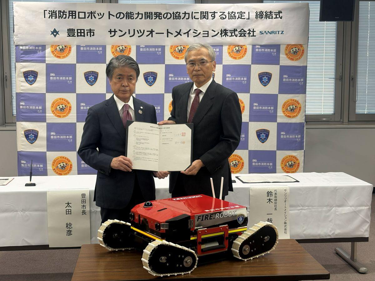 協定書を手にする太田市長（左）と鈴木社長（右）と消防用ロボット（手前）。