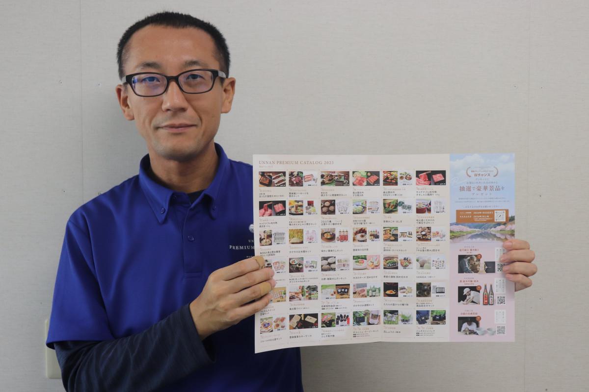 「雲南プレミアムカタログ2025」の商品一覧を手に購入を呼びかける担当の槇野さん
