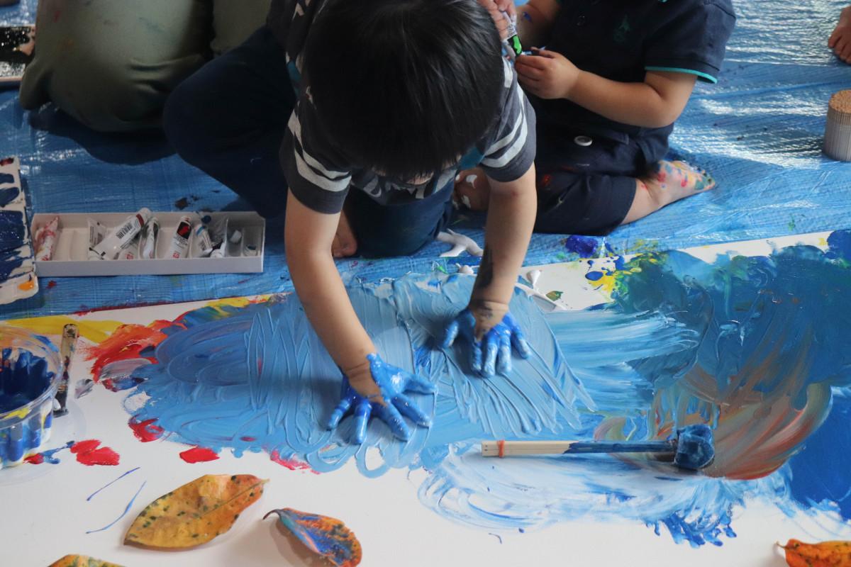 大きな白いべニア板に絵の具をつけた両手で思いっきり描く子ども