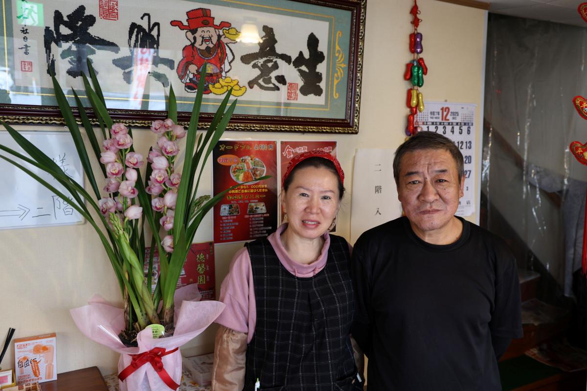 店頭に飾られた営業再開を祝う花と店主の孟さん（左）、調理を担当する于さん（右）