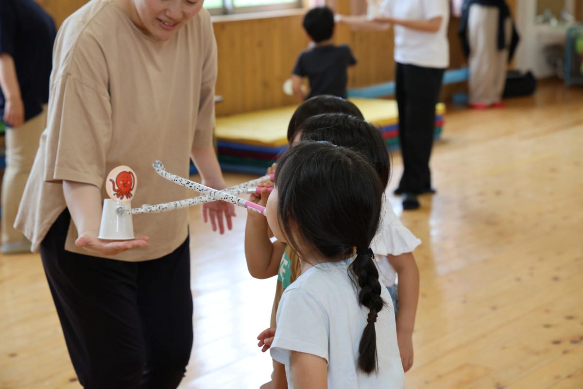 保育士の持つ紙コップをピロピロで落とす園児たち
