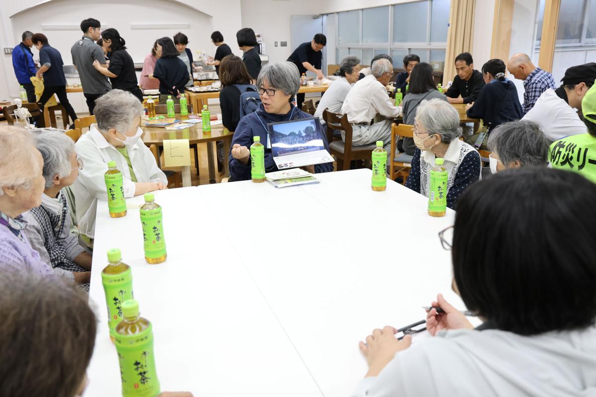 岡山県での豪雨災害の様子と支援の状況を説明する石原さんと熱心に聞き入る地域の人たち