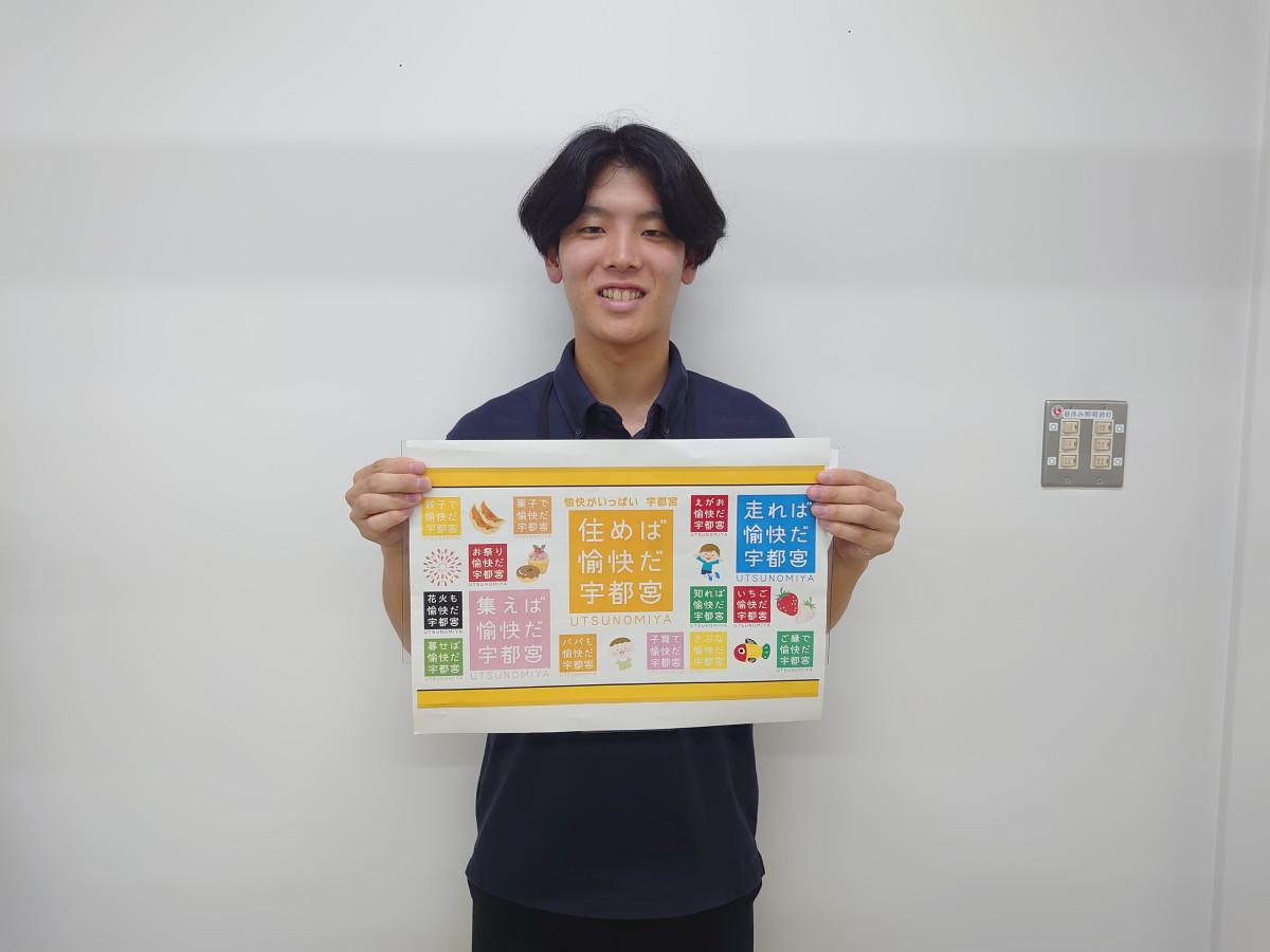 オリジナル愉快ロゴマークを手にする担当の青柳大輝さん