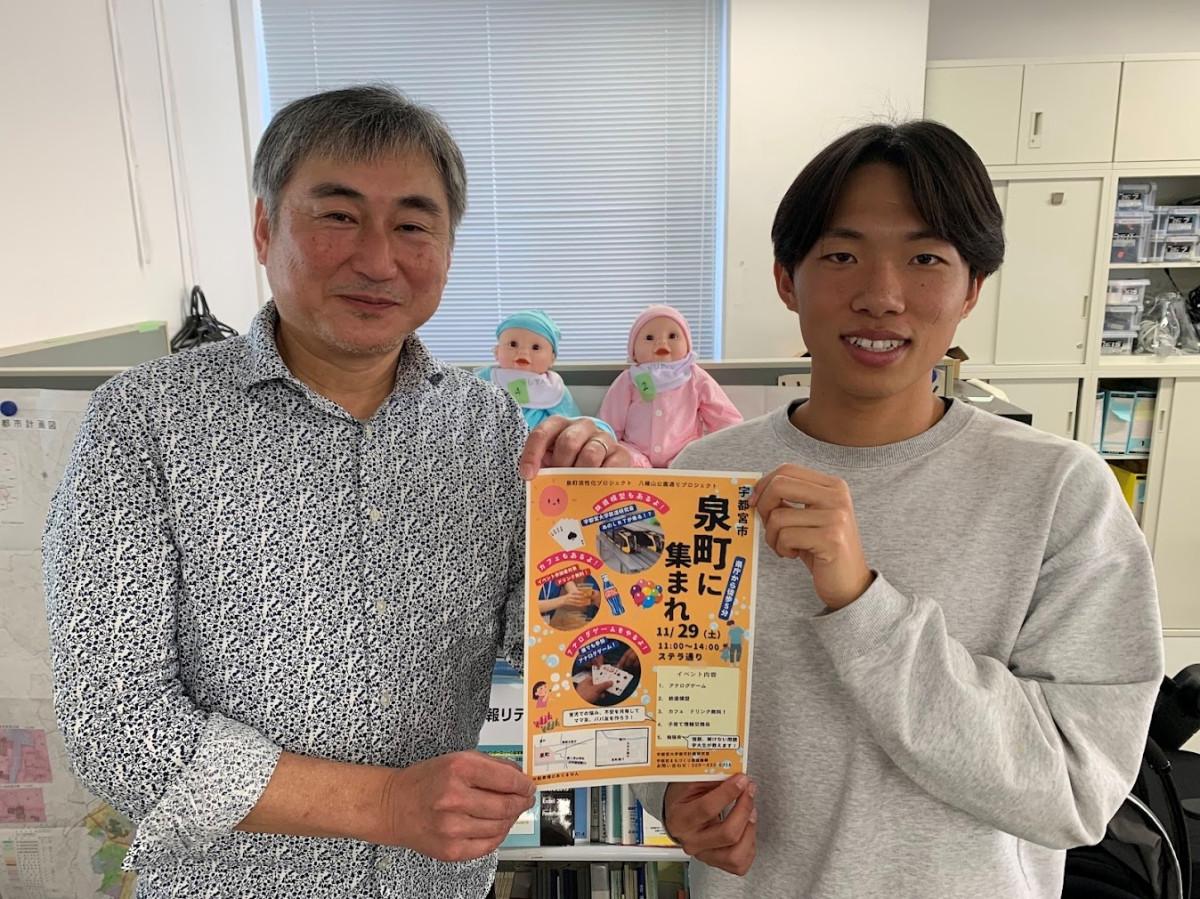 「泉町に集まれ」のチラシを手にする（左から）大森教授と学生代表の良知蒼大さん（地域デザイン科学部4年）